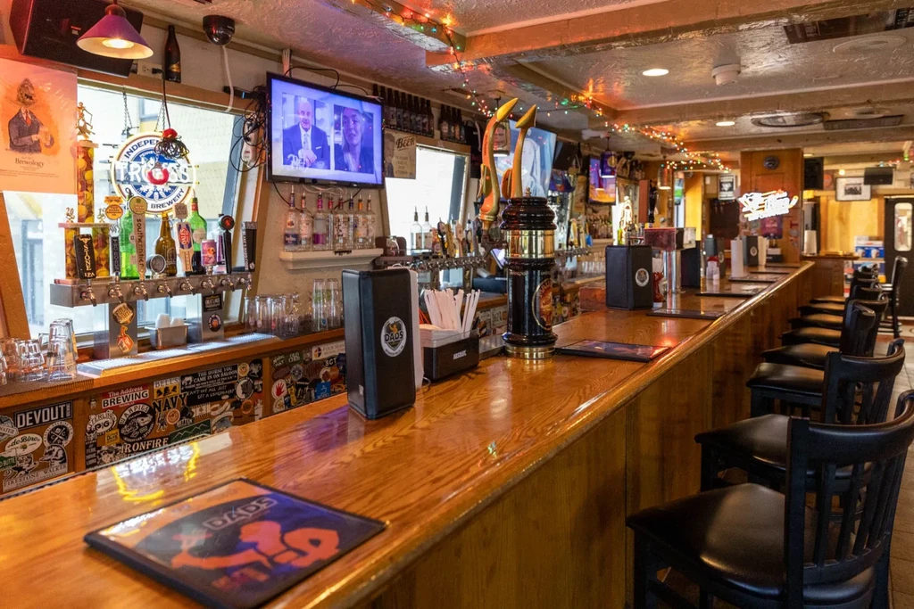 Warm, empty bar interior with stocked wooden counter, stools, and 'DADS'.