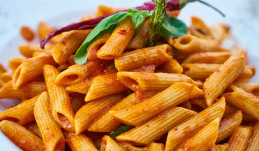 Penne pasta in tomato-chili sauce, garnished with basil and rosemary.