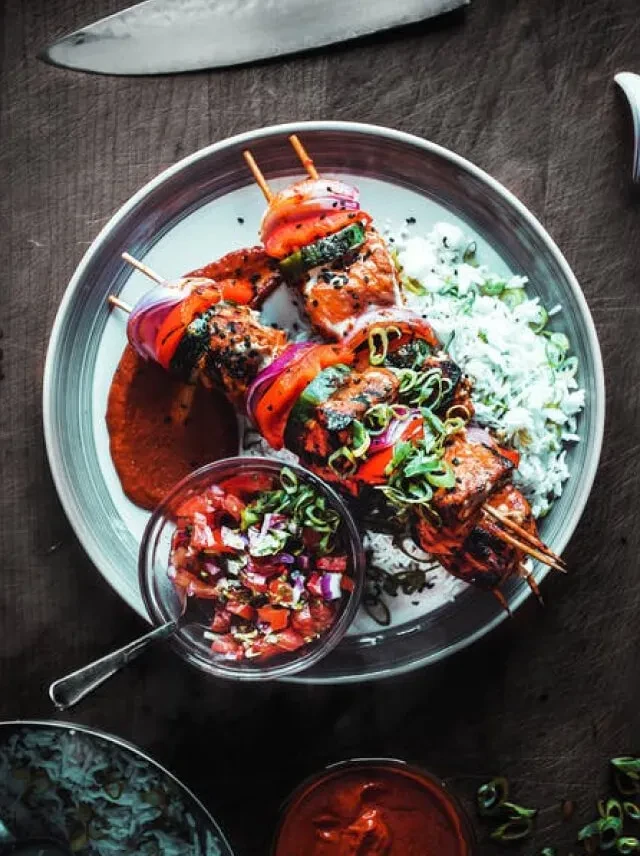 Two grilled meat and vegetable skewers with rice, red sauce, and salsa.