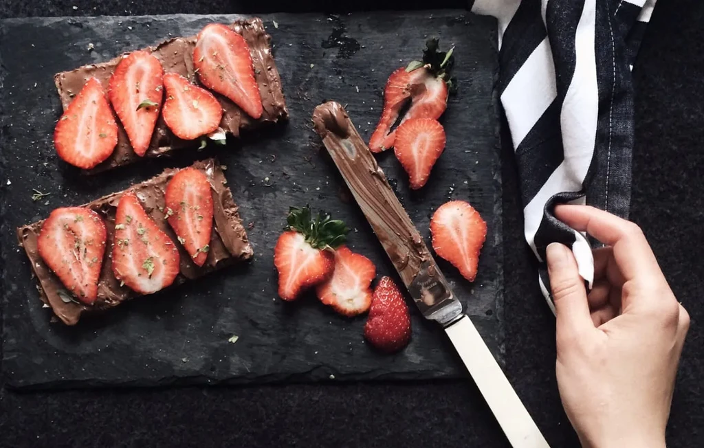 Flat lay: Two chocolate spread toasts with strawberries and herbs.