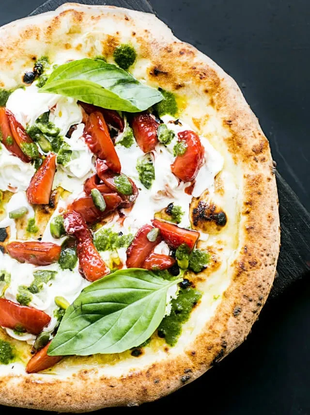 Neapolitan pizza with burrata, roasted peppers, pesto, and basil.