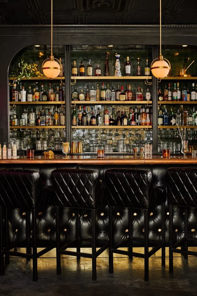 Luxurious bar interior, fully stocked with liquor bottles and leather stools.