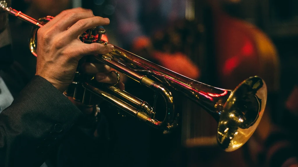 Close-up of hands playing a gleaming golden trumpet in dim light.