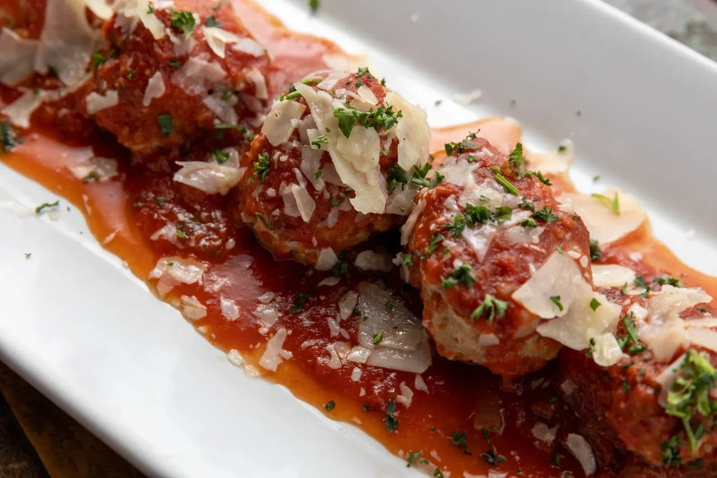 Close-up of meatballs in tomato sauce with cheese and herbs on a white dish.
