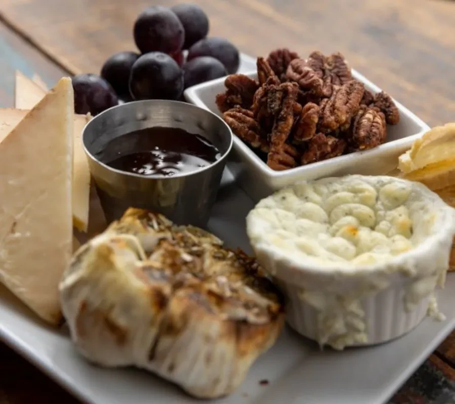 Platter of cheese, grapes, nuts, and dips on a rustic table.