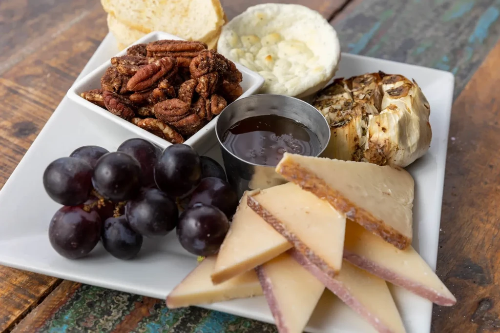 White rectangular charcuterie platter with cheese, dark grapes, spiced pecans, roasted garlic.