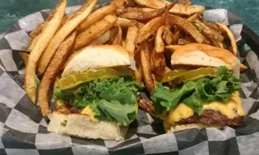 Two sliders with cheese, lettuce, pickles, and golden french fries.