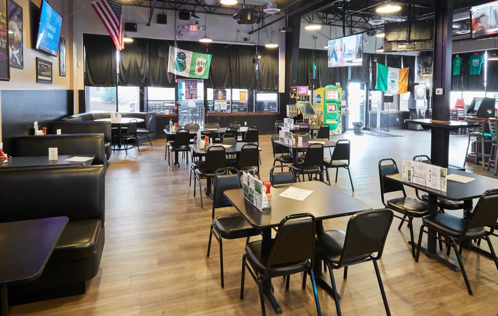 Empty sports bar dining area with booths, tables, TVs, and arcade games.
