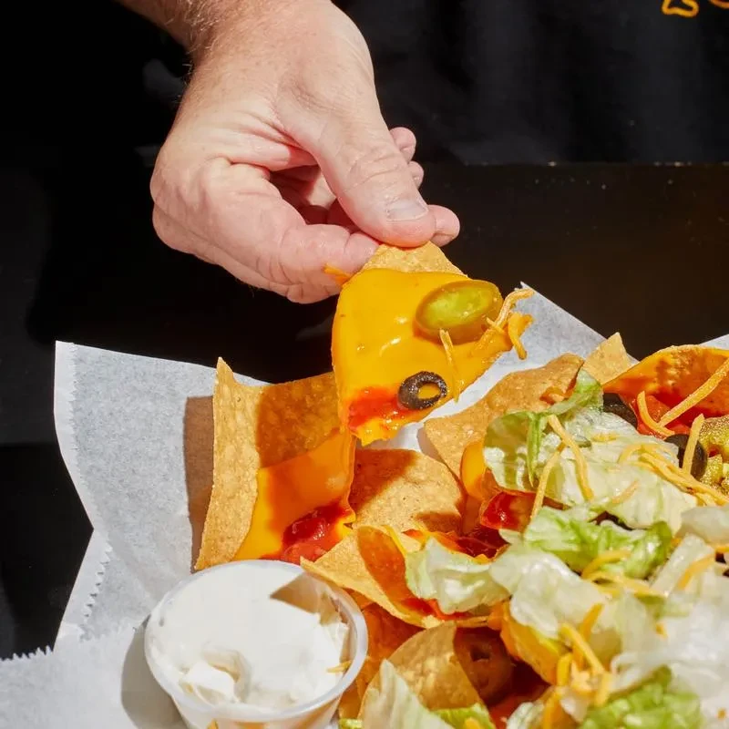 Hand lifting a nacho chip with cheese, jalapeño, and olive.