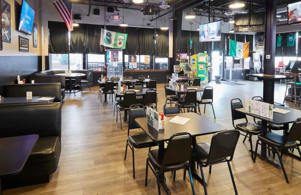 Empty sports bar interior with booths, arcade games, TVs, and flags.