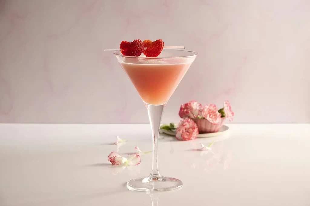 Pink cocktail in martini glass, garnished with heart-shaped strawberries.