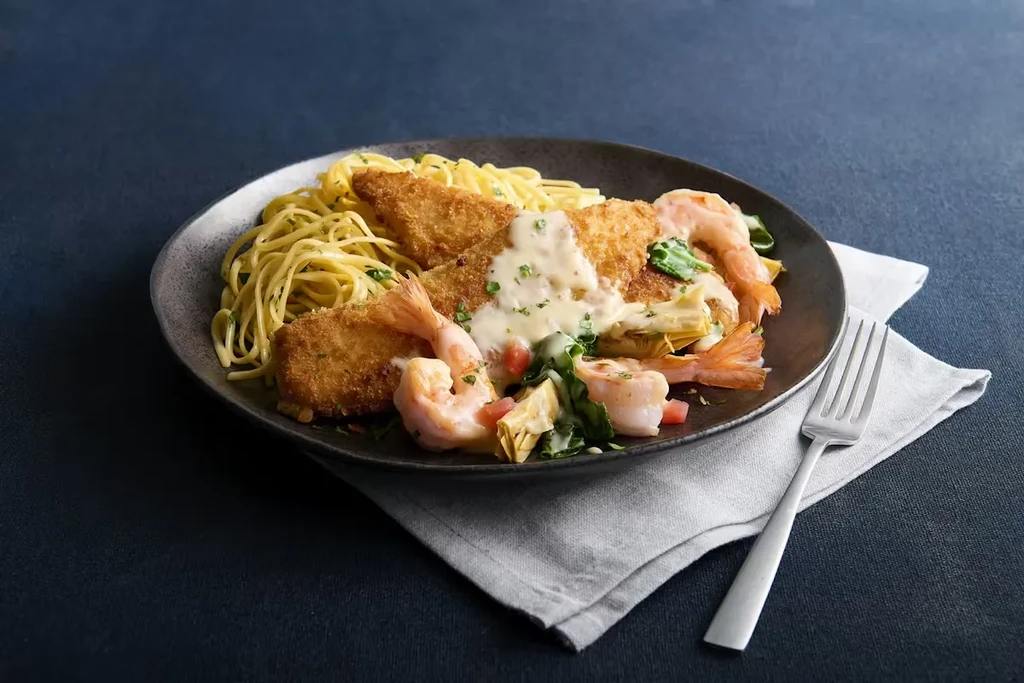 Plated spaghetti, breaded fish, shrimp, creamy sauce, artichokes, and tomatoes.