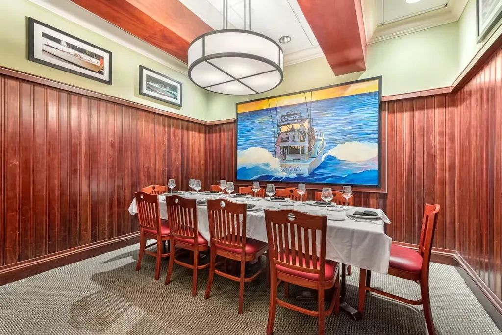 Private dining room with wood paneling, fishing boat art, and set table.