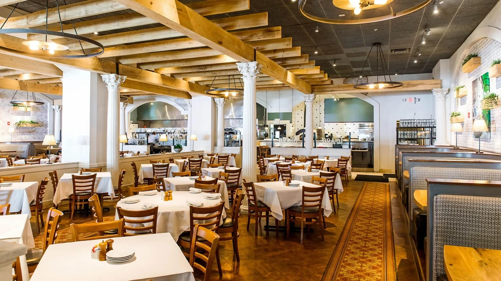 Restaurant dining room with white-clothed tables, patterned booths, and open kitchen.