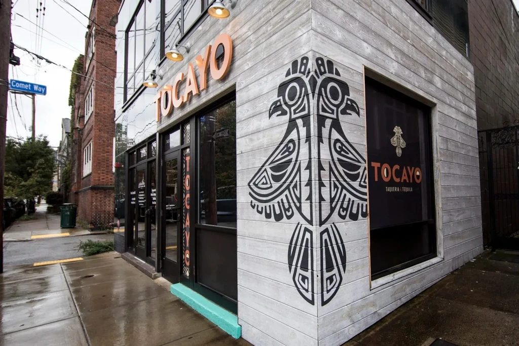 Modern "TOCAYO Taqueria" exterior with wood paneling and bird graphic.