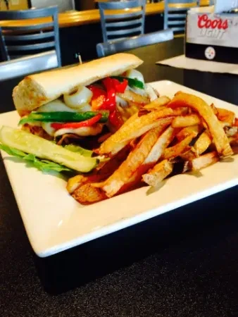 Close-up of a cheesesteak sandwich, golden fries, pickle, and lettuce.