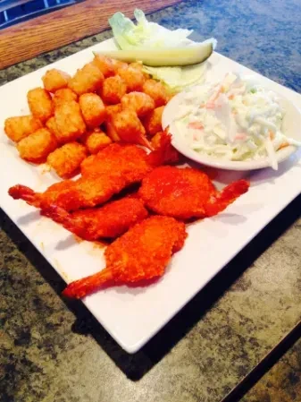 Fried shrimp, tater tots, coleslaw, pickle, and lettuce on a plate.
