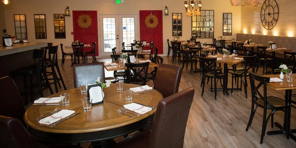 Empty rustic-modern restaurant dining area with set tables and bar.