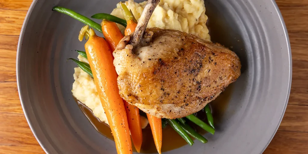 Plated roasted poultry, mashed potatoes, carrots, string beans, and gravy.