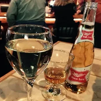 Wine, shot, and Miller High Life beer on a dim restaurant table.