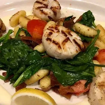 Grilled scallops, gnocchi, spinach, cherry tomatoes, and lemon on a plate.