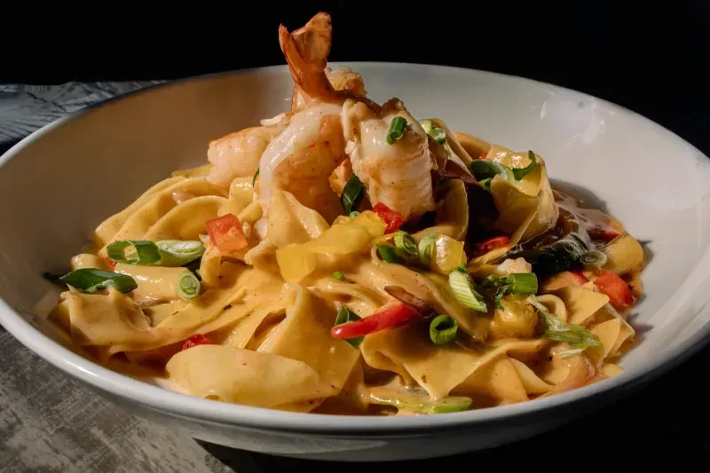Creamy shrimp pasta dish with orange sauce, peppers, and green onions.