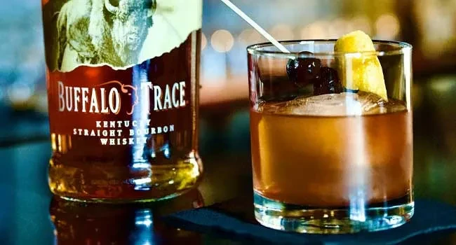 Buffalo Trace bourbon bottle and a bourbon cocktail with cherries and lemon.