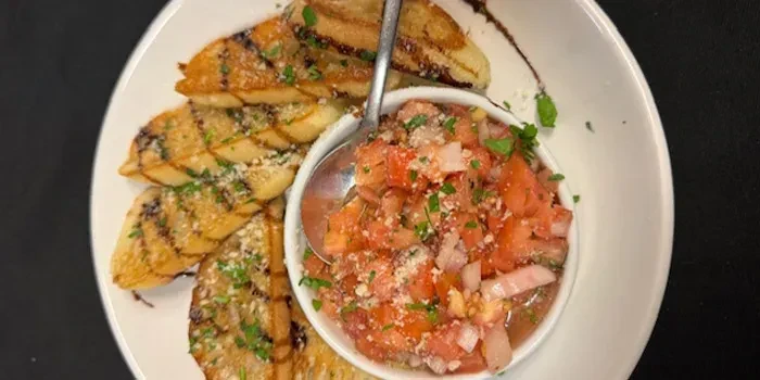 White plate with grilled crostini, bruschetta topping, and spoon.