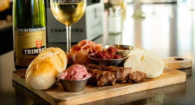 Charcuterie board with bread, meats, cheese, sauces, and white wine.