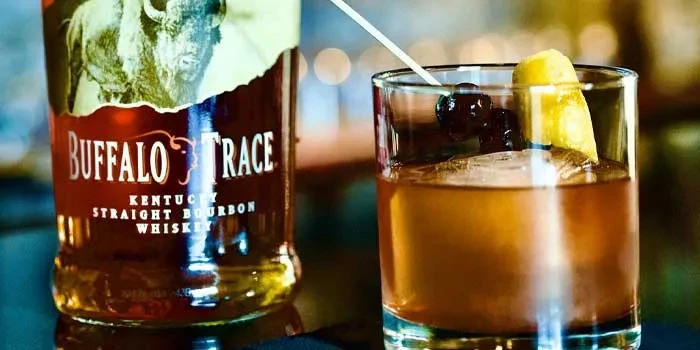 Buffalo Trace bourbon bottle next to Old Fashioned with cherry and lemon.