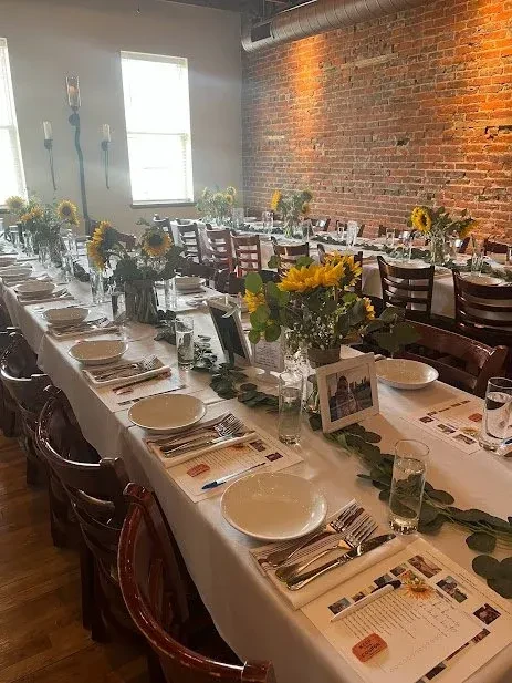 Restaurant dining table with sunflowers, eucalyptus, and place settings, brick wall.