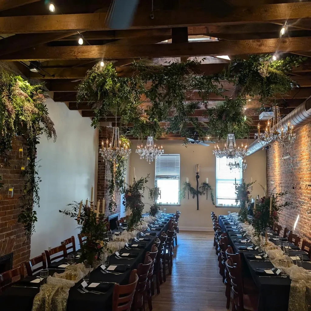 Long formal dining hall with decorated tables, plants, and chandeliers.