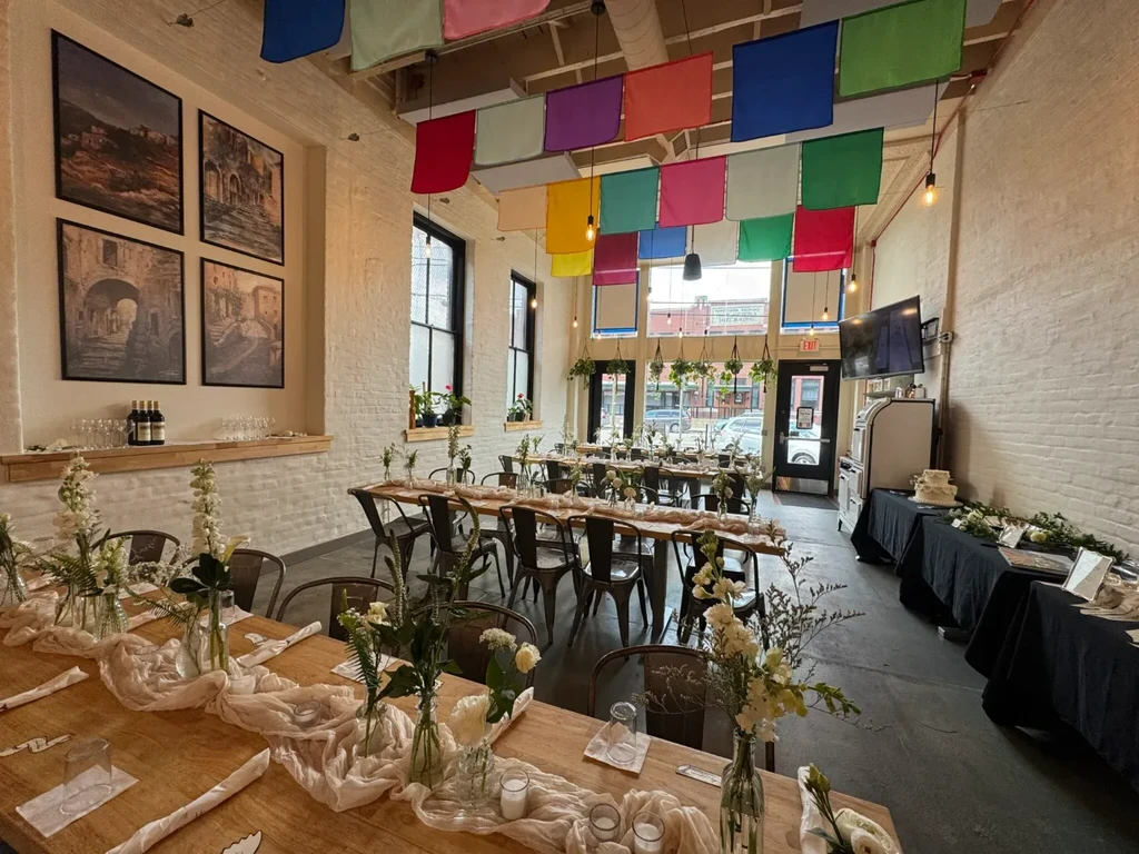 Decorated event venue with brick walls, colorful fabric ceiling, and rustic tables.