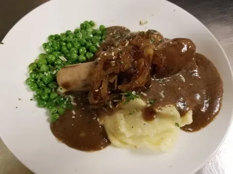 Sausage, mashed potatoes, peas, gravy, and caramelized onions on a plate.