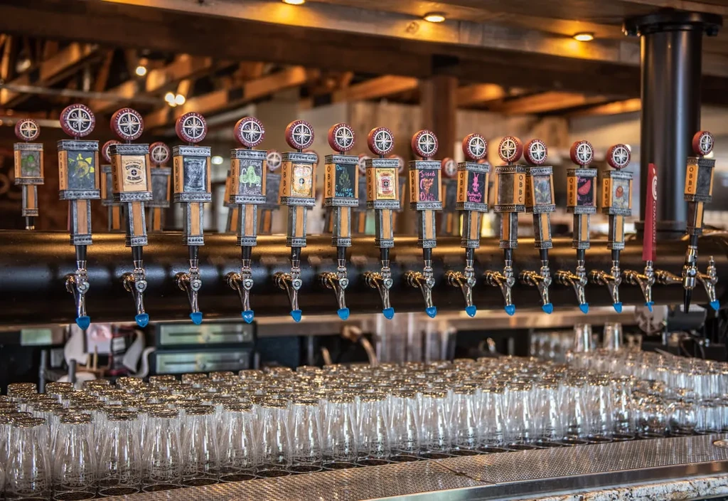Many unique beer taps above clean inverted glasses in a bar.