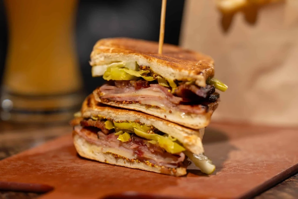 Grilled Cuban sandwich, cut in half, with meats, cheese, and pickles.