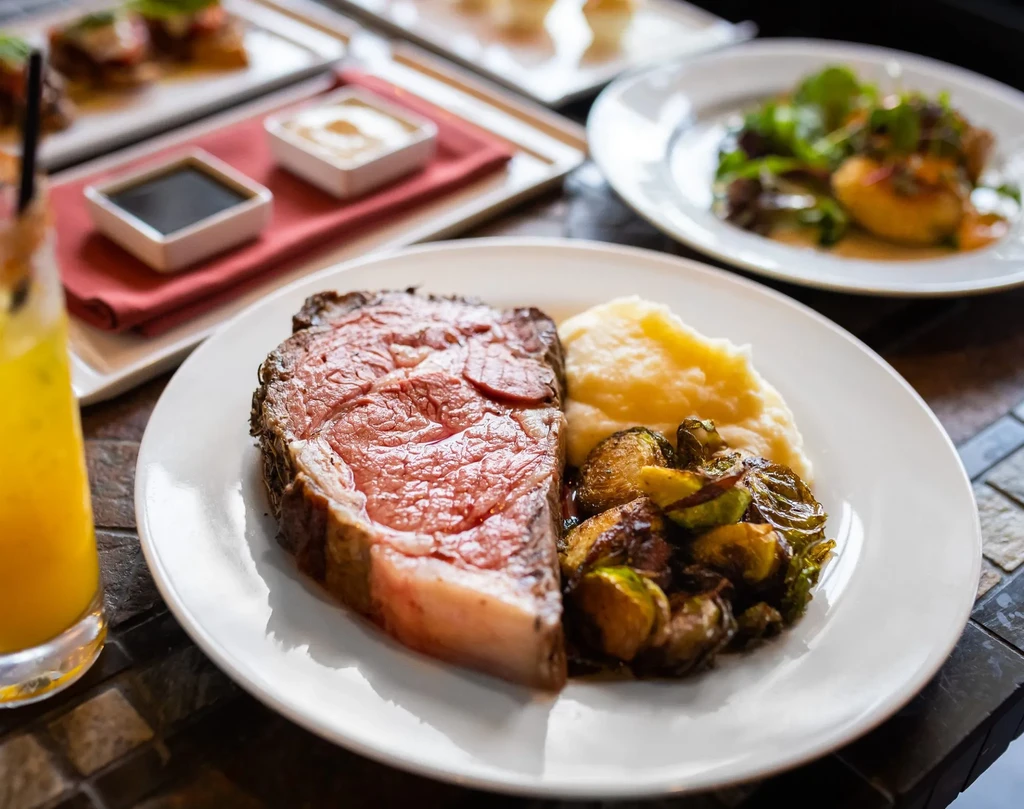 Medium-rare prime rib, mashed potatoes, and roasted Brussels sprouts on a plate.