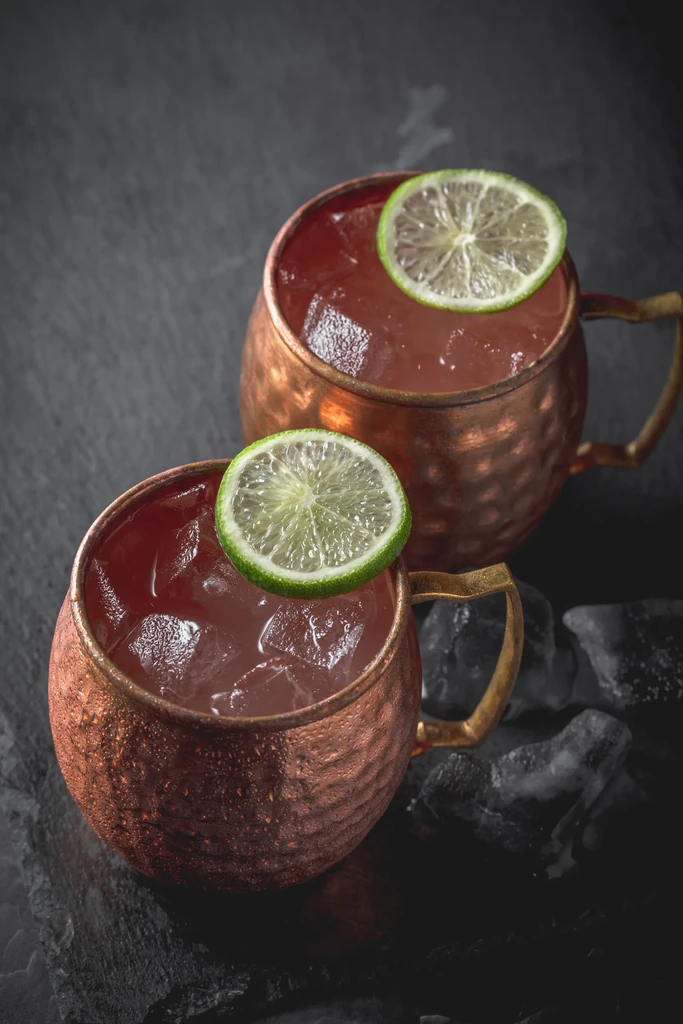 Two hammered copper mugs with cold red drinks, ice, and lime.
