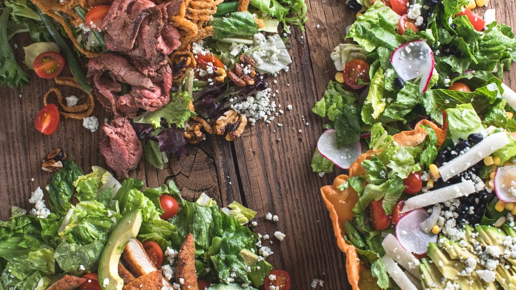 Overhead shot of three distinct gourmet salads on a rustic wooden table.