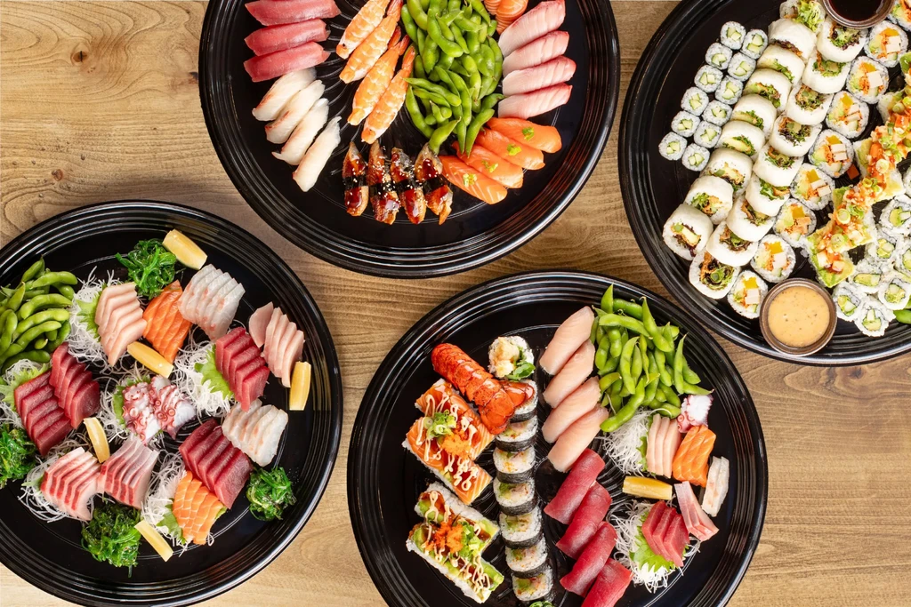 Overhead shot of four platters of varied Japanese sushi and sashimi.