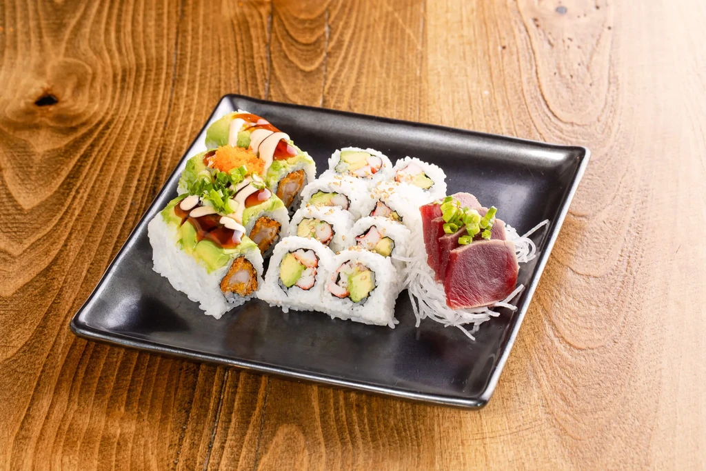 Black plate featuring sushi rolls with avocado and seared tuna sashimi.