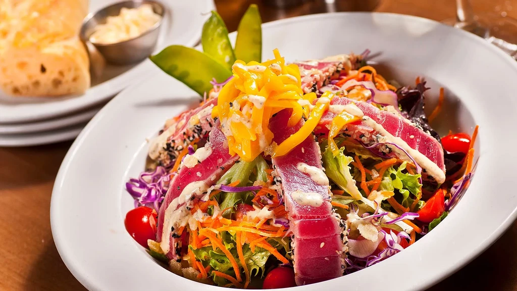 Seared tuna salad with mixed greens, colorful vegetables, and dressing.