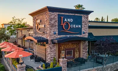 Warmly lit LAND and OCEAN restaurant exterior with patio and fire pits.