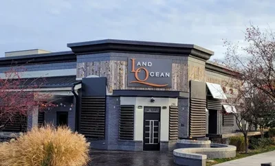 Exterior of modern two-story "LAND AND OCEAN" restaurant building with bare trees.