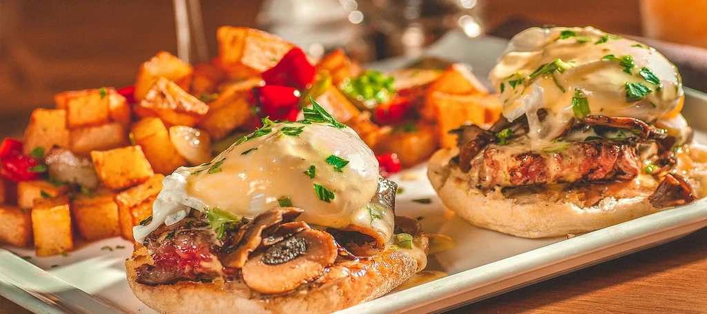 Two steak Benedicts with hollandaise, mushrooms, and home fries.