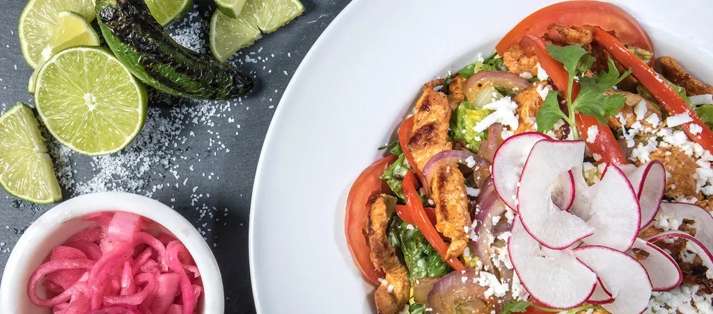 Overhead: Grilled chicken salad with cheese, vegetables, lime, and pickled onions.