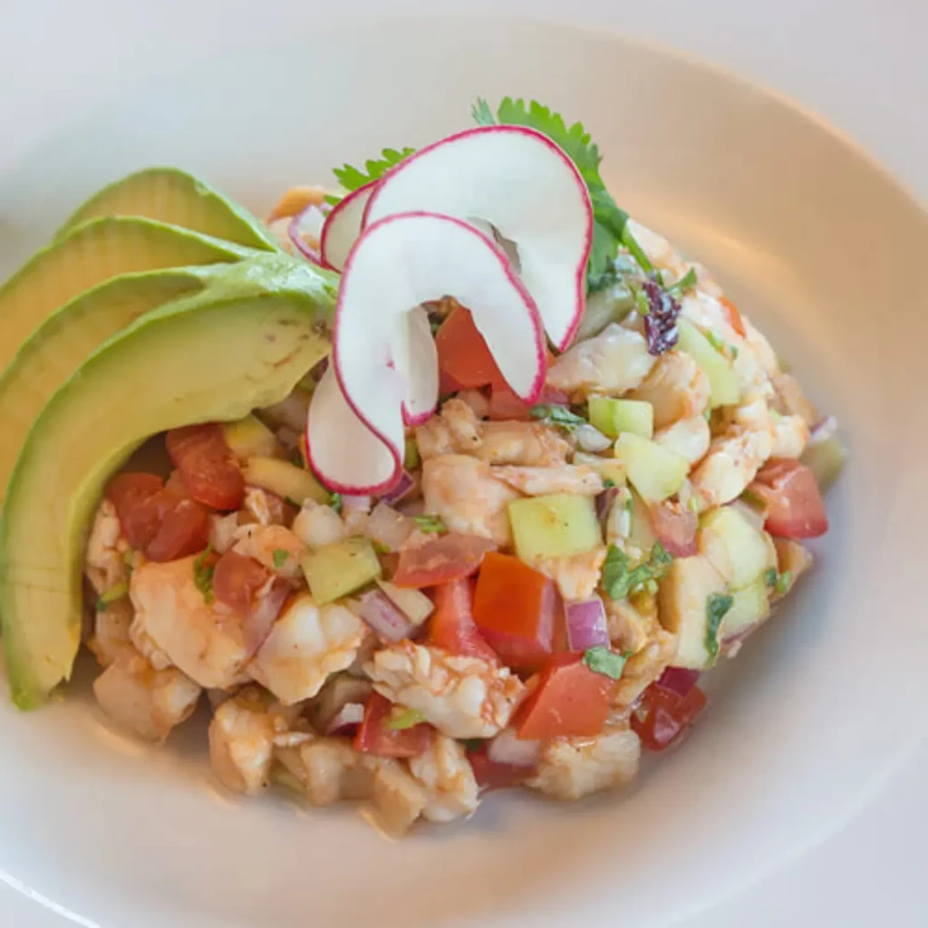 Artfully arranged ceviche with shrimp, tomatoes, cucumber, avocado, and radish.