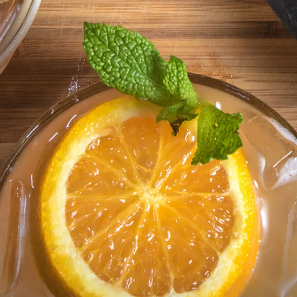 Orange drink with orange slice, mint, and ice on wood.