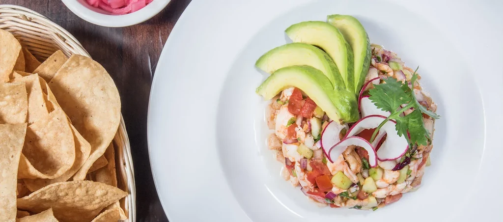 Overhead: Plated seafood salad with avocado, radish, chips, pink condiment.