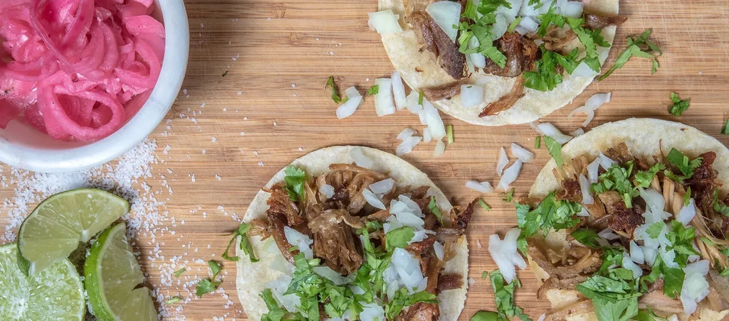 Three meat tacos with cilantro, onions, limes, and pickled onions.